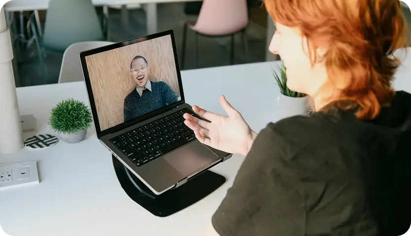 woman sitting at a table with a laptop and a video chat