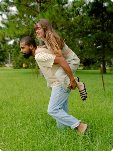Couple enjoying a playful moment in a green park, promoting a healthy lifestyle before insurance verification.