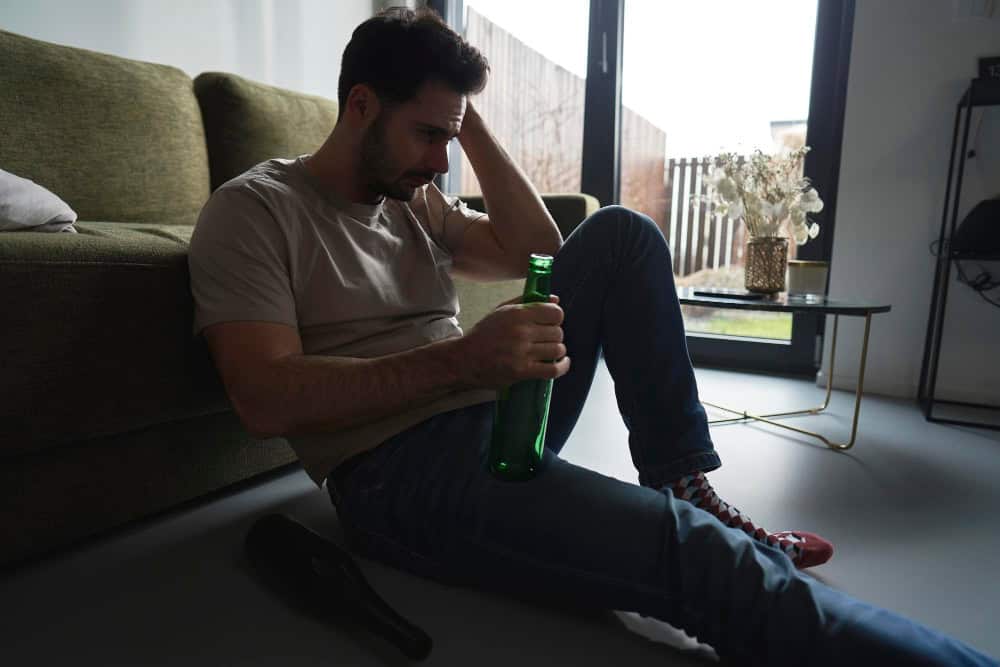 Intoxicated man sitting on the floor among empty bottles, representing alcohol use and panic attack risks.