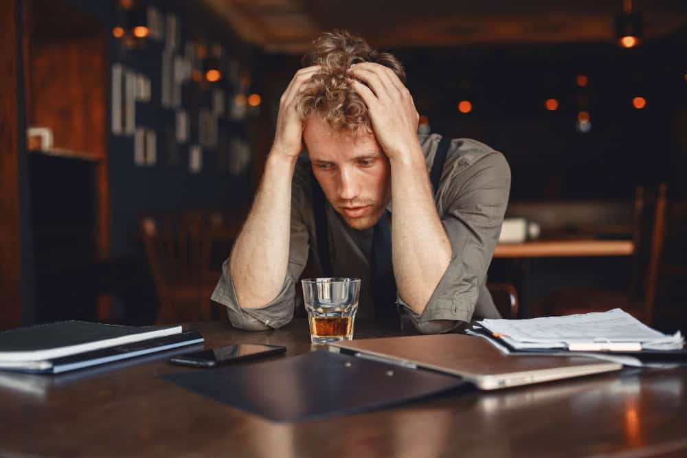 Man drinking whiskey at a cluttered desk, illustrating the connection between alcohol and panic attacks.